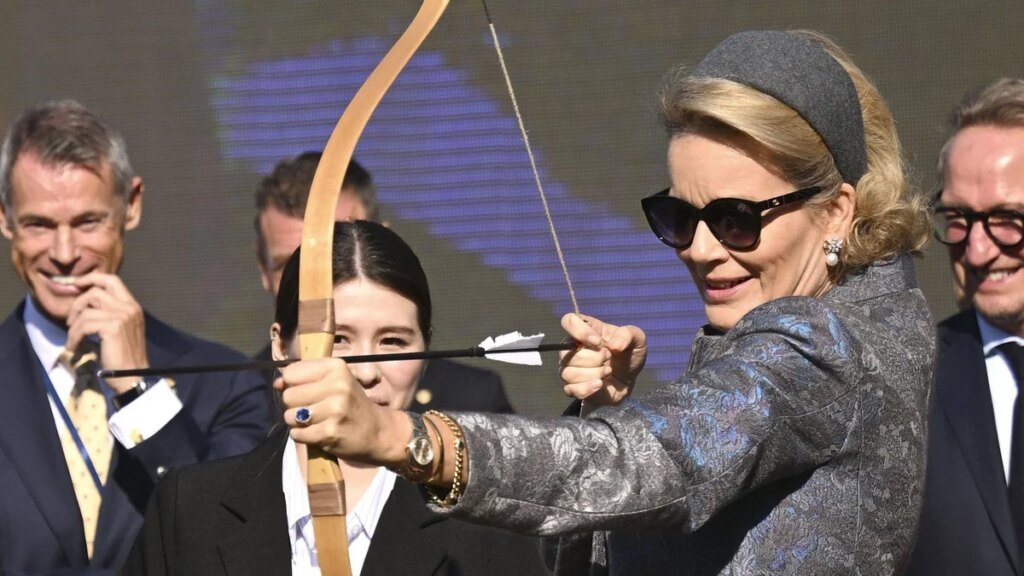 La reina Mathilde prueba el tiro con arco con tacones y un elegante abrigo floral mientras el rey Felipe observa con una sonrisa